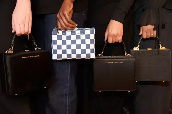 Four hands holding different designer handbags by Brandon Blackwood