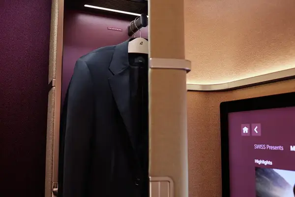 A closet in a Swiss firstclass suite with a suit hanging inside next to an entertainment screen