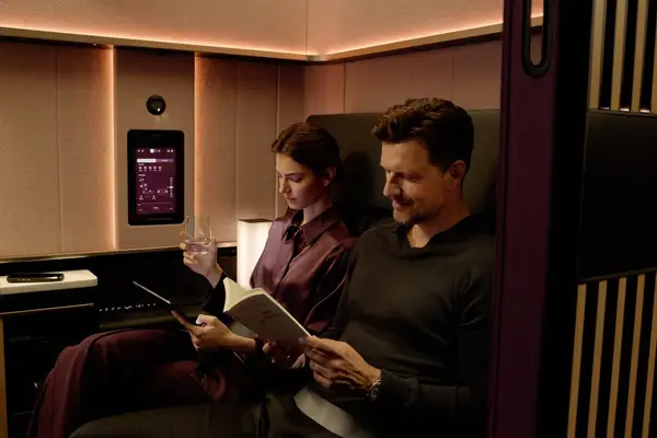A man and woman seated in a premium aircraft suite reading and relaxing