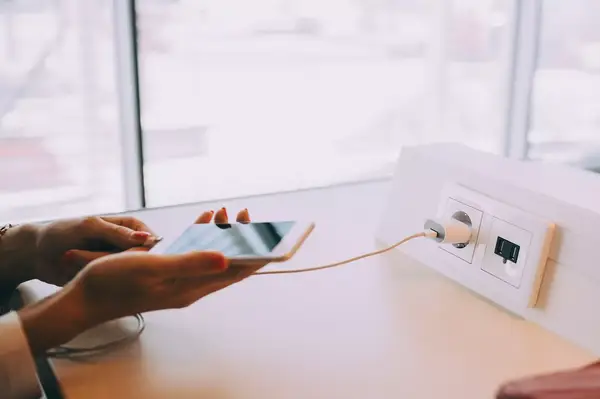 A person holding a smartphone while it charges at an airport charging station