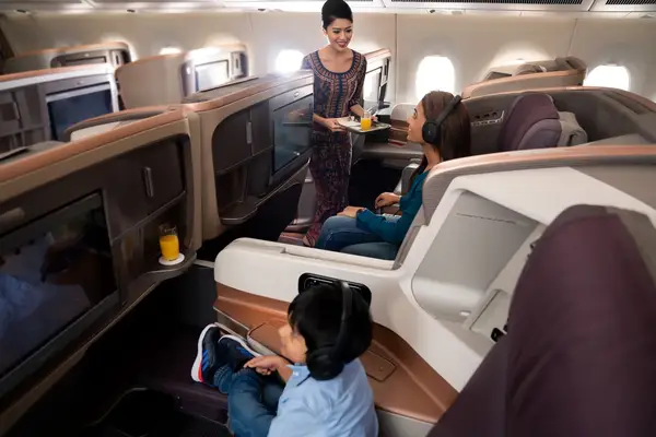 A flight attendant serving a beverage to a passenger seated in a premium airline cabin with child seated nearby