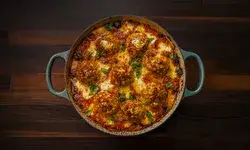 A dish with chicken parm meatballs topped with sauce and cheese presented in a round baking dish with handles