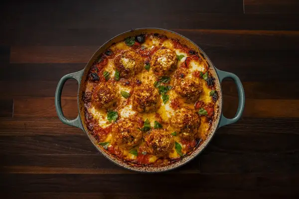 A dish with chicken parm meatballs topped with sauce and cheese presented in a round baking dish with handles