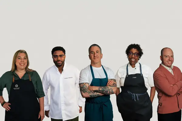 Group of five chefs posing wearing aprons or uniforms standing side by side