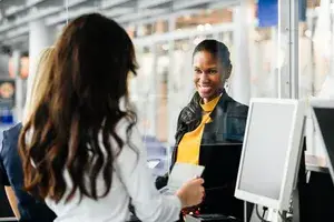 A woman behind a counter checking a passport presented by another woman