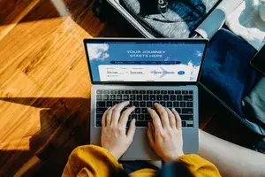 hands searching on laptop for flight deals sitting on the floor