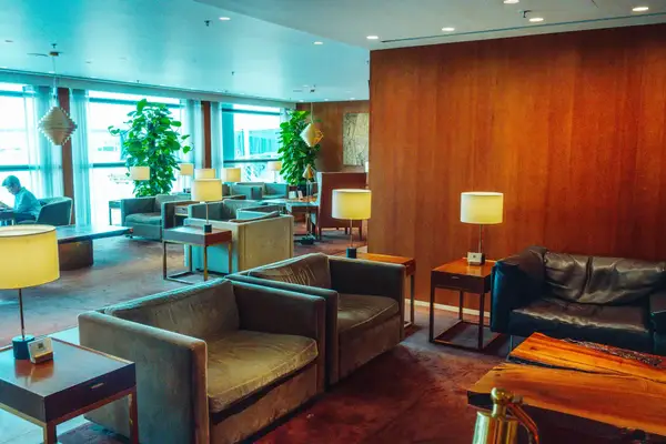 Seating area in a lounge with armchairs tables and lamps positioned near large windows