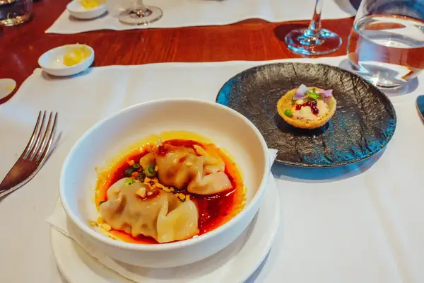 A bowl of dumplings with sauce a small tart on a plate and table settings