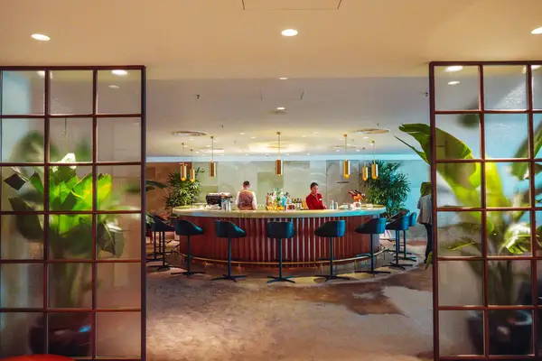 A lounge area with a central bar stools and plants with two individuals seated at the counter