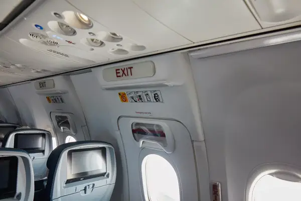 Interior view of an airplane cabin focused on the emergency exit row and related signage