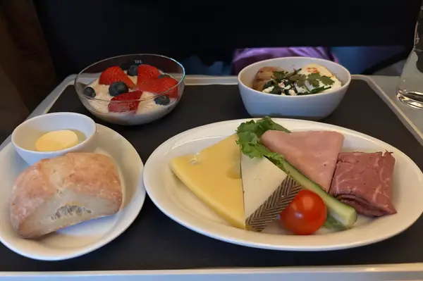 An inflight meal consisting of cheese, bread, cold cuts, and yogurt with berries