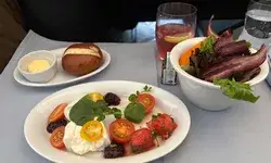 A meal served on an airplane includes a salad, bread roll, and a dish with burrata cheese and tomatoes