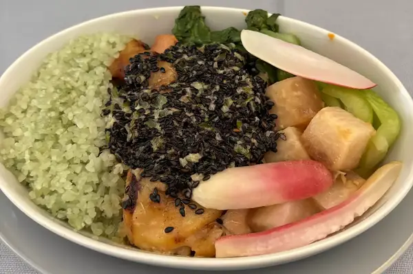 Bowl of food containing grains, vegetables, and a topping of black seeds