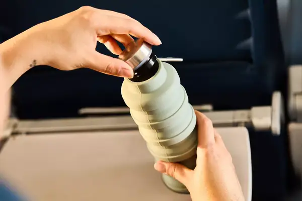 Hands opening a collapsible water bottle on an airplane tray table, highlighted to demonstrate its practicality for travel