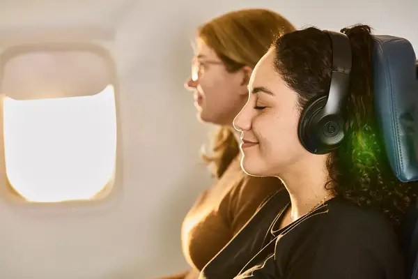 Two passengers seated on an airplane, one wearing headphones
