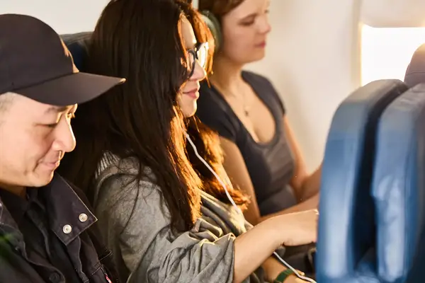 Three people seated side by side on an airplane, one interacting with the controls on the armrest