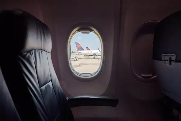 View of airplanes parked near an airport from the window of an airplane cabin with empty seats visible