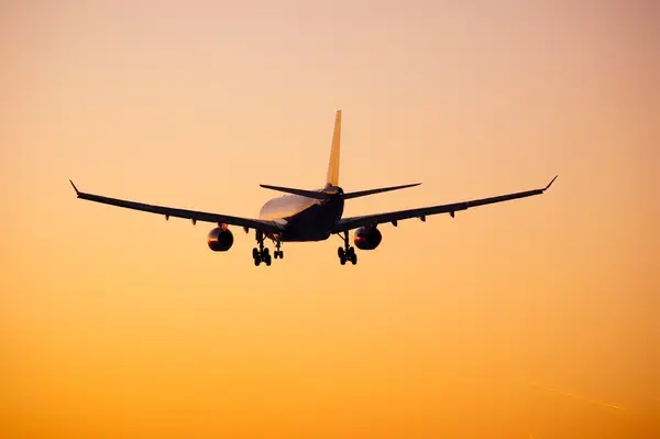 An airplane in flight, seen from behind, during sunset