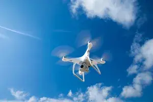 A white quadcopter drone flying against a background of blue sky with scattered clouds