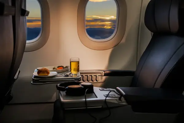 Airplane seat with meal tray on a table sunset visible through window
