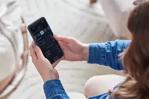 Person holding a smartphone displaying a flight booking application interface, seated indoors