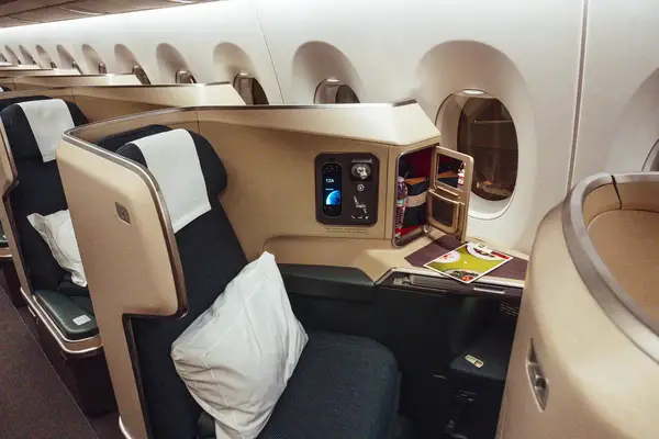 Firstclass airline seat equipped with a pillow and remote console along with a tray featuring magazines and refreshments