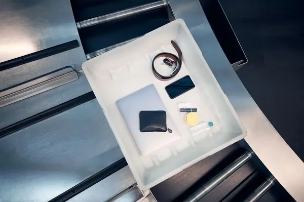 Items including a laptop, phone, wallet, belt, and toiletries in a TSA security tray on a conveyor belt