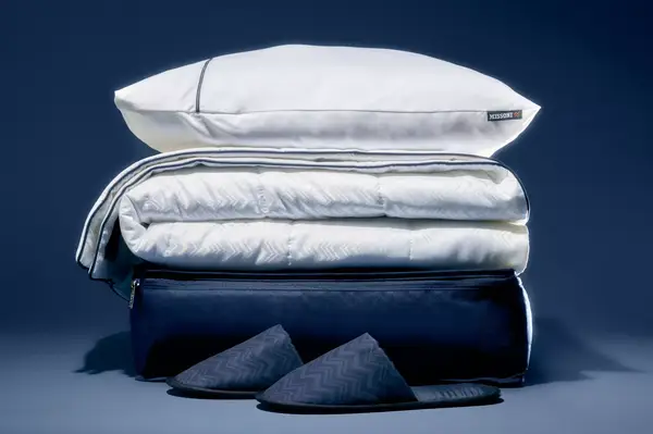 Stacked bedding items including pillows, folded linens, and slippers on a dark background