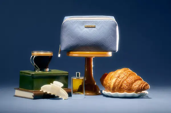 A Missoni bag displayed with a cup of espresso, a croissant, and a bottle of fragrance