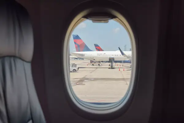 View through an airplane window showing parked aircraft on the tarmac at an airport