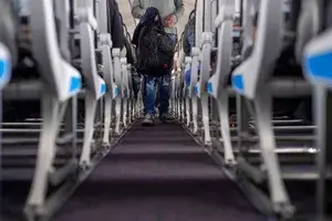 Low angle selective focus shot of unrecognisable people boarding a plane, walking up the aisle. The plane is going to the UK from France.
