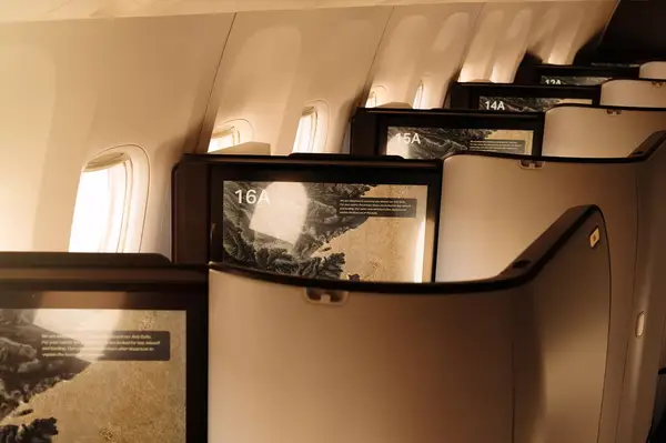 Interior view of business class seats on a Cathay Pacific airplane showing partitions and seat numbers