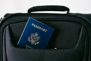 A passport partially visible in the pocket of a black carry-on bag