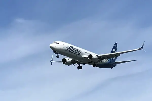 An Alaska Airlines plane in flight against a blue sky approaching for landing