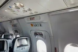 Interior view of an airplane cabin focused on the emergency exit row and related signage