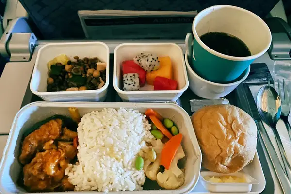 Airplane meal with rice chicken curry fruit vegetable sides bread and a cup of drink on a tray