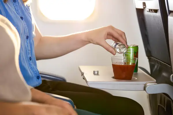 Person pouring alcohol into a drink on an airplane tray table green can and cup present