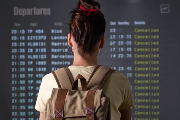 Person with a backpack facing a departures board with cancelled flights