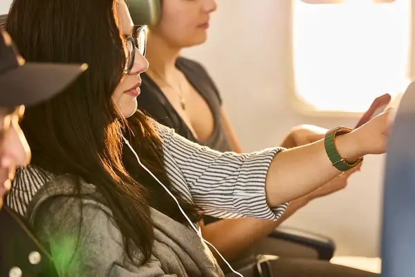 Passengers sitting in an airplane one wearing earbuds and another reaching outwards