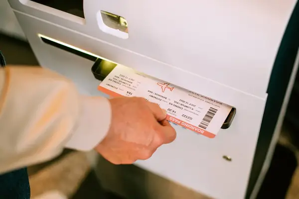 A hand retrieves a boarding pass from a selfservice kiosk