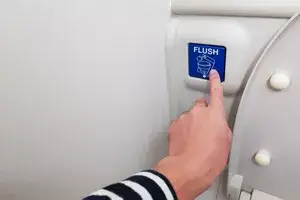 Asian men hand pressing blue flush button sign at the air plane lavatory to clean after use. Interior toilet design to match with small space inside the aircraft.