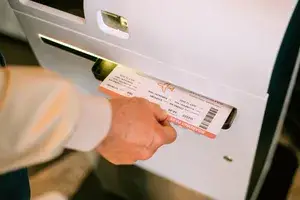 A hand retrieves a boarding pass from a selfservice kiosk