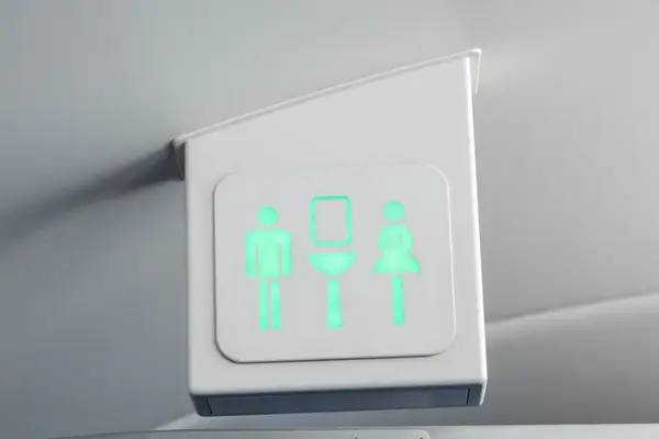Lit bathroom indicator sign inside an airplane showing a man a sink and a woman