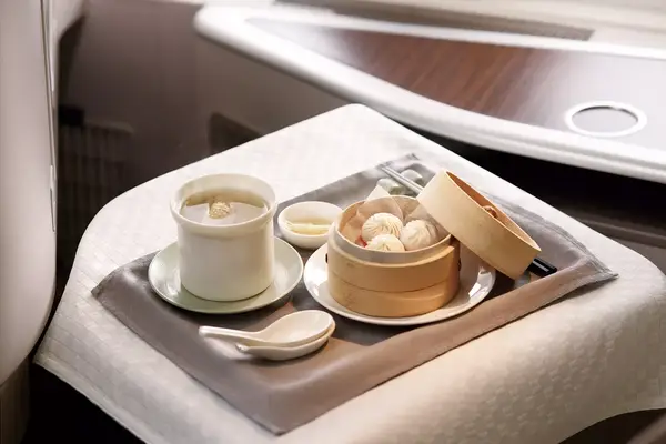 Tray of food with dumpling steamer, soup, and a small dish, presented in a refined setting