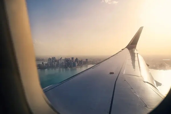 View of an airplane wing with a distant cityscape and water body visible during flight