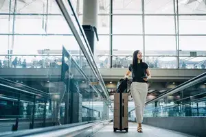 Person walking on a moving walkway at an airport with luggage in hand