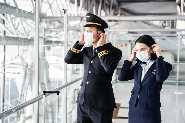 A pilot and flight attendant wearing face masks standing in an airport terminal