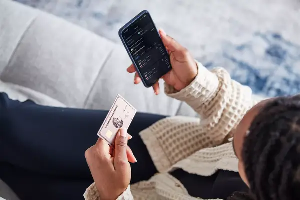 Person holding a smartphone displaying flight prices and a credit card seated on a couch