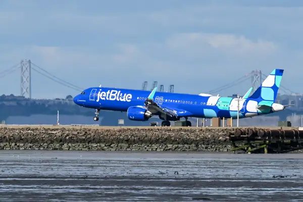 JetBlue airplane taxiing on a runway with a bridge in the background