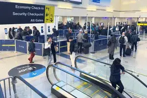 Crowded security checkpoint area in an airport with travelers standing in lines and escalators in the foreground